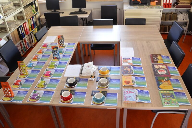 Na zdjęciu stoły, na których leżą dyplomy, gry "Story cubes", filiżanki, czekolady i książki. 