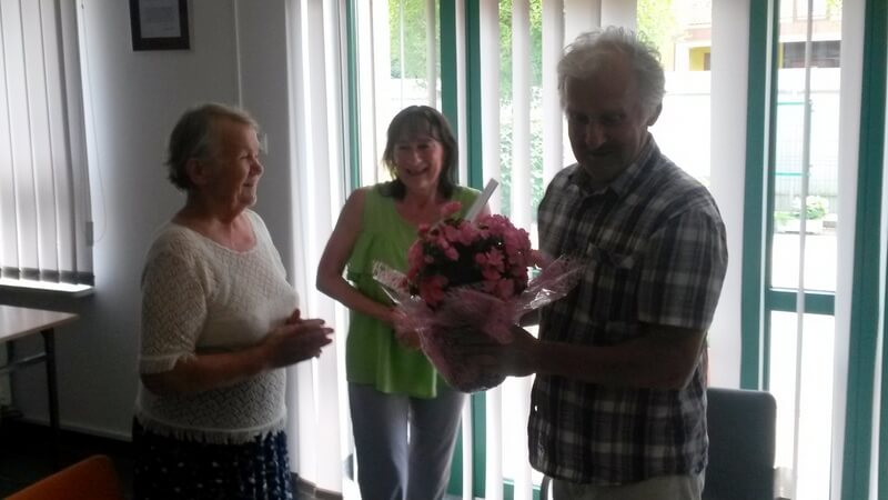 Dwie kobiety wręczyły kwiaty mężczyźnie. W tle drzwi. 