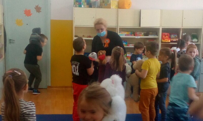 Prowadząca zajęcia tańczy wraz z dziećmi i pluszowymi misiami. W tle widać meble i zabawki dziecięce.