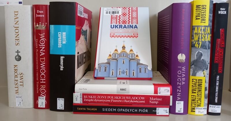 Siedem książek stojących, widoczna jedna okładka: Katarzyna Łoza: Ukraina; trzy książki leżące, widoczne grzbiety.