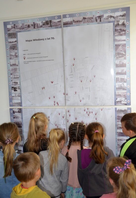 Grupa dzieci przypatruje się mapie Włodawy z lat 70. Dzieci skierowane są plecami do fotografa.