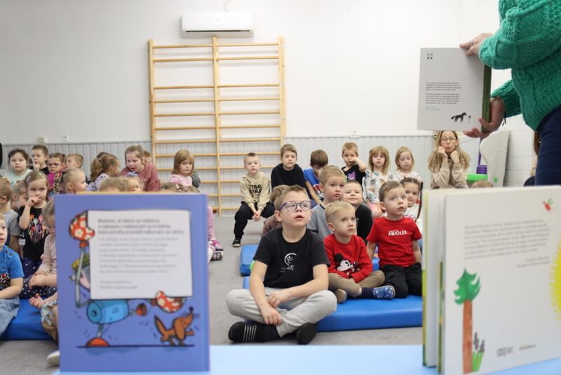 Na pierwszym planie widzimy okładki książek, które są częścią wyprawki. W oddali widzimy grupę przedszkolaków.