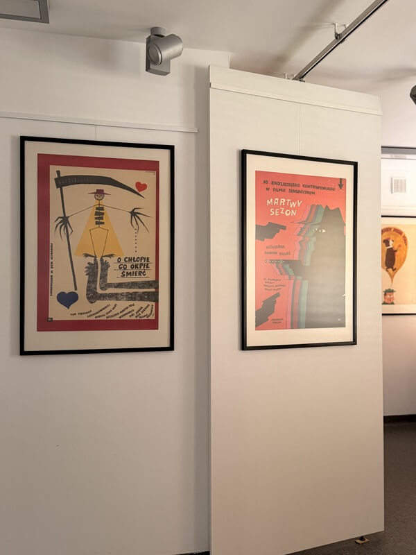 Wnętrze galerii. Po lewej plakat do czeskiej komedii „O chłopie, co okpił śmierć”, a po prawej do radzieckiego filmu szpiegowskiego „Martwy sezon”